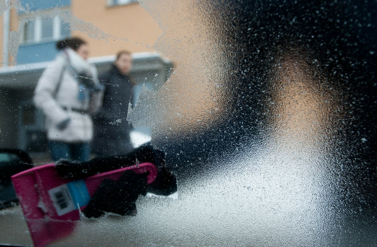 Na zdjęciu osoba zdrapująca mróz z szyby samochodu