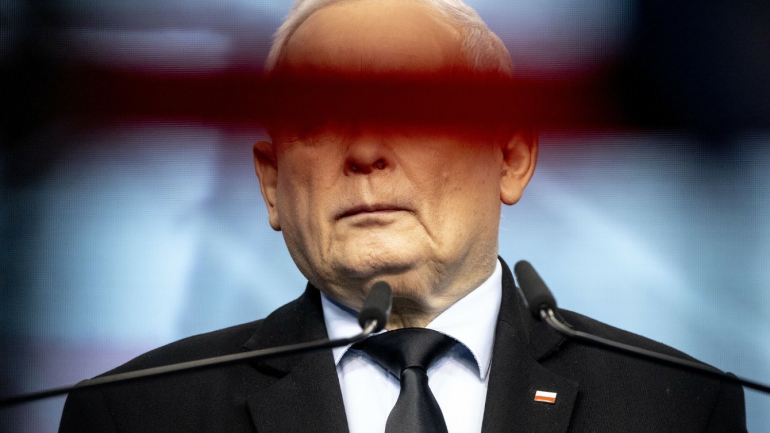 Prezes PiS Jarosław Kaczyński stojący przy mikrofonie. Zdjęcie zrobione jest w taki sposób, że jego oczy są niewidoczne, bo przesłania je pozioma przeszkoda.
