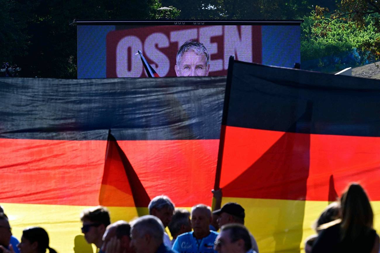 Na zdjęciu wiec Bjoerna Hoeckego z AfD. Polityk widoczny w tle na ekranie za wielkimi niemieckimi flagami.