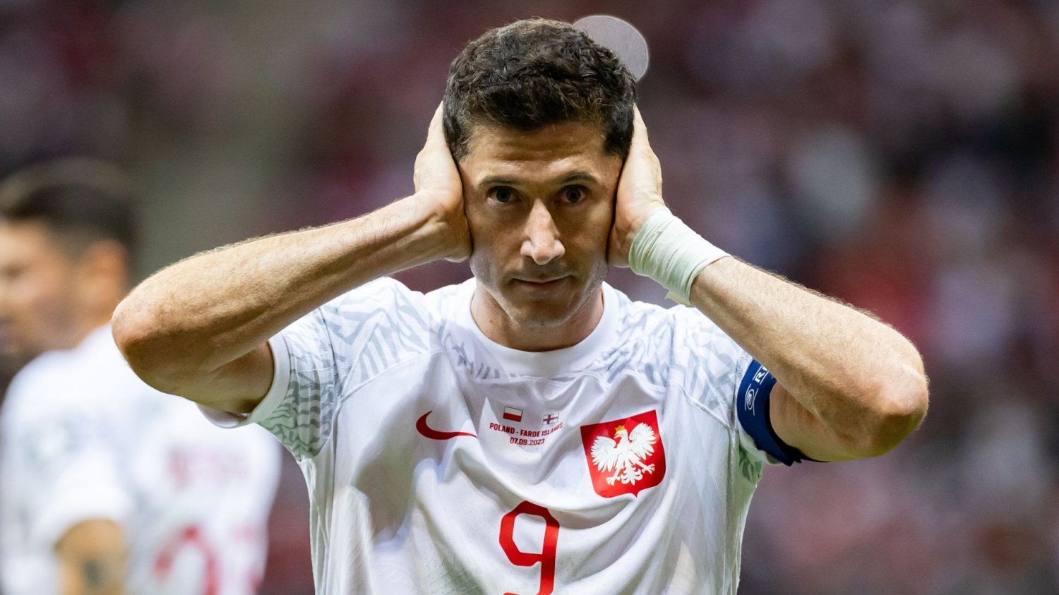 Robert Lewandowski zasłaniający uszy dłońmi.