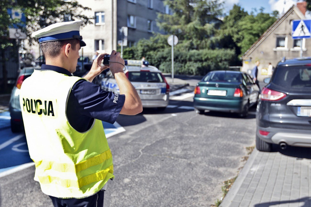 Na zdjęciu policjant drogówki robi zdjęcie, aby wystawić mandat za złe parkowanie.