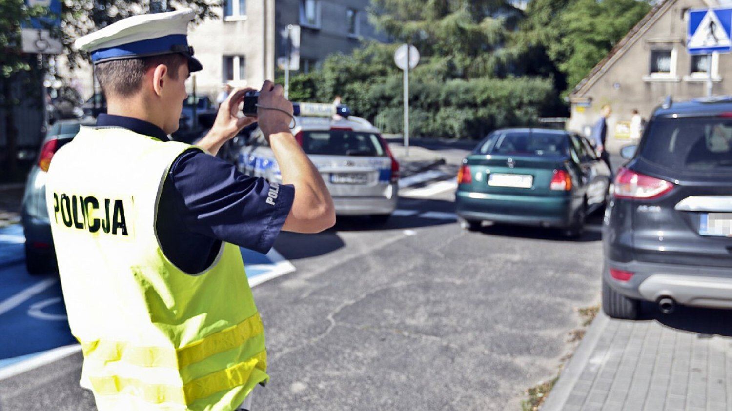Policja i straż miejska wlepiają mandaty za złamanie znaków zakazu parkowania B-37 i B-38. Na zdjęciu policjant drogówki robi zdjęcie, aby wystawić mandat za złe parkowanie.