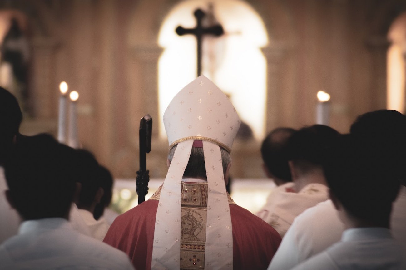 Biskup stojący tyłem otoczony księżmi.