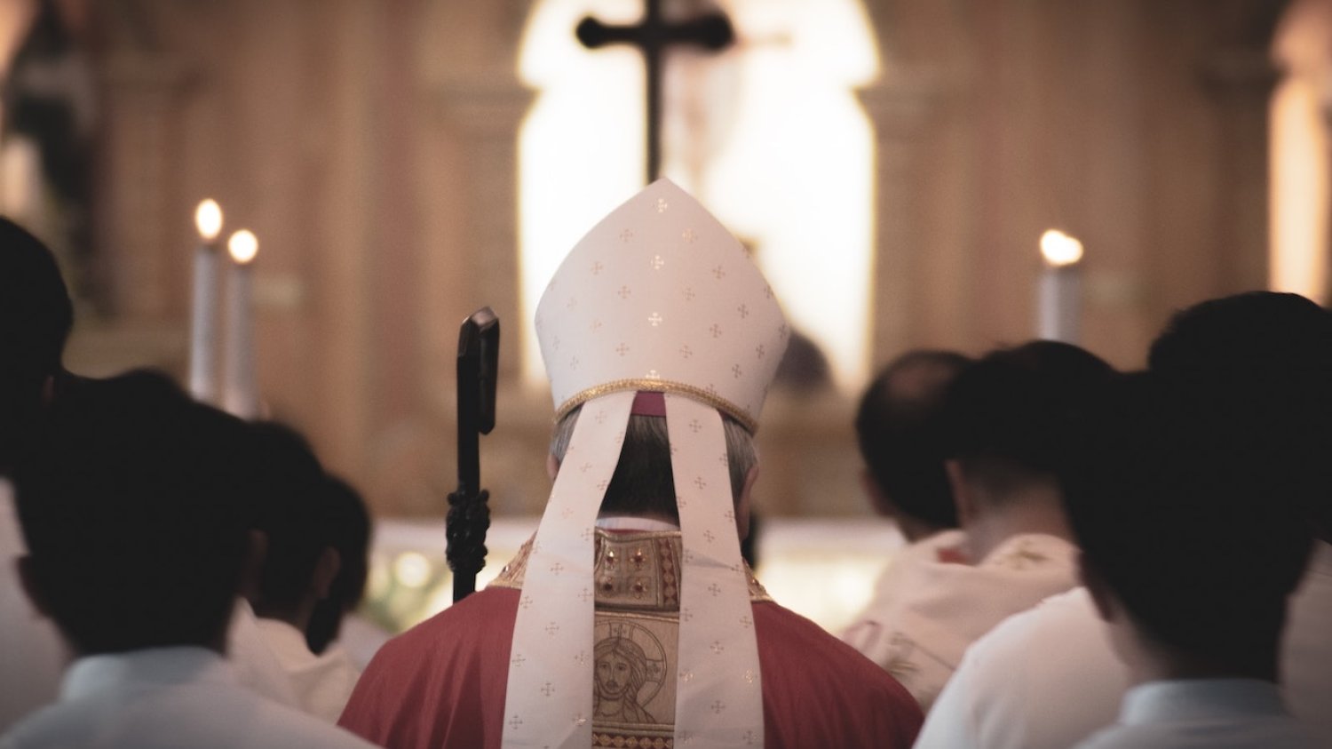 Biskup stojący tyłem otoczony księżmi.
