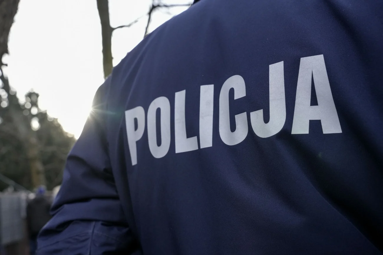 W Warszawie w koszu na śmieci znaleziono ciało psa. Sprawcy szuka policja. Plecy funkcjonariusza w mundurze z napisem "Policja".