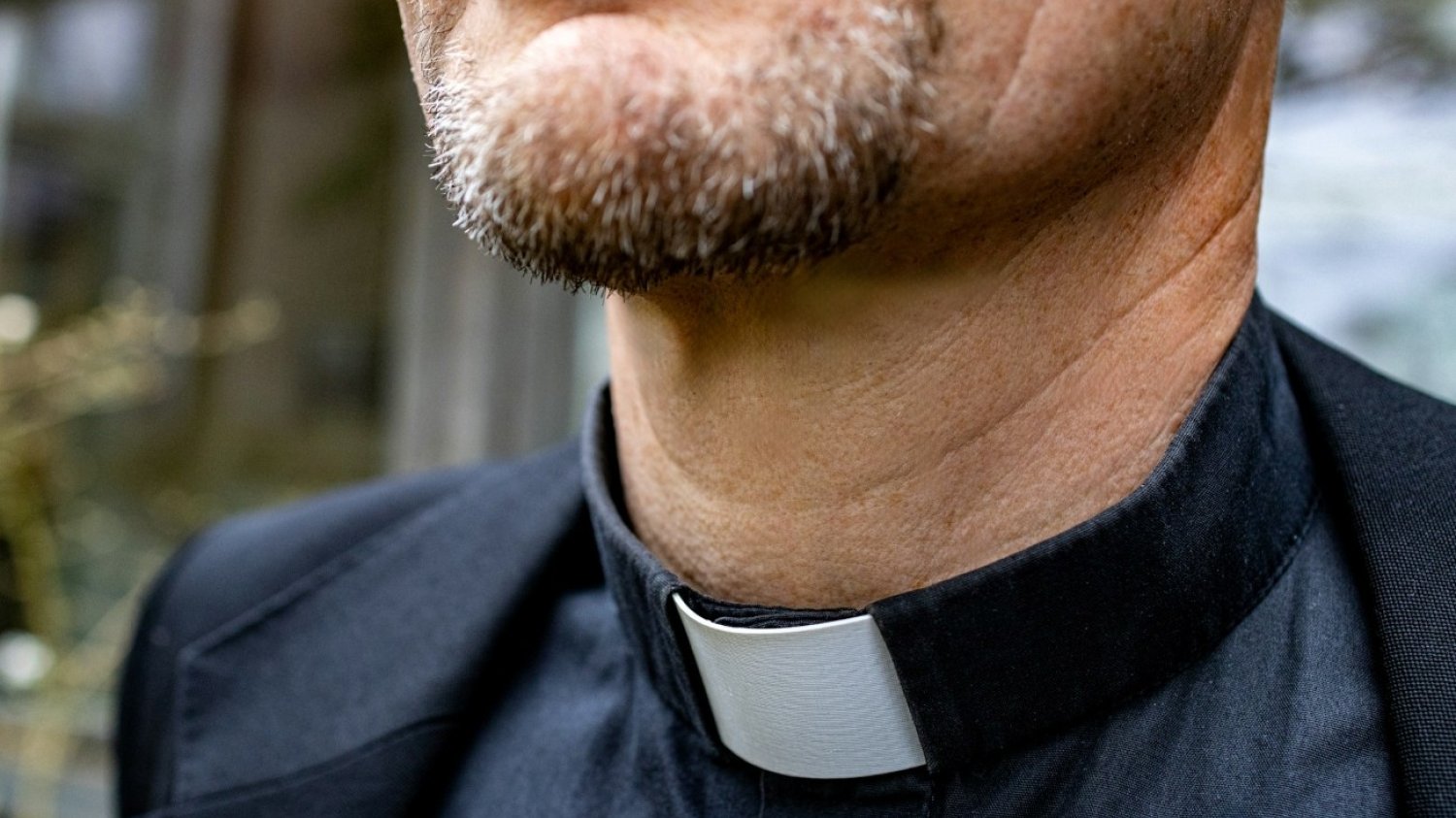 Mężczyzna w ubraniu księdza skadrowany od ust do piersi.