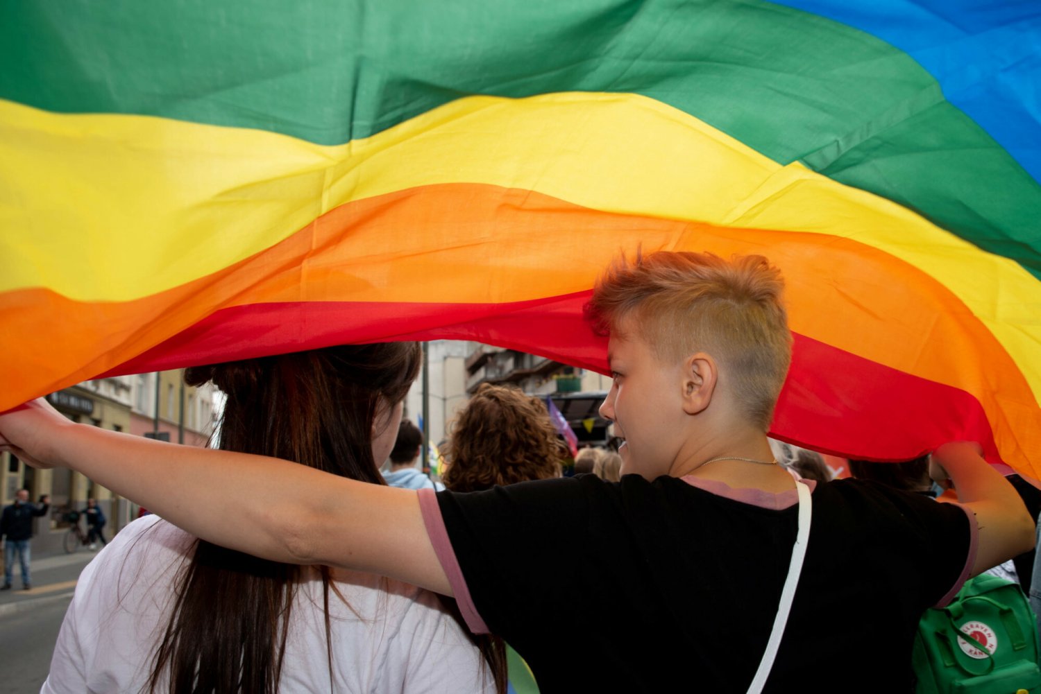 Dwie osoby pod tęczową flagą na Paradzie Równości