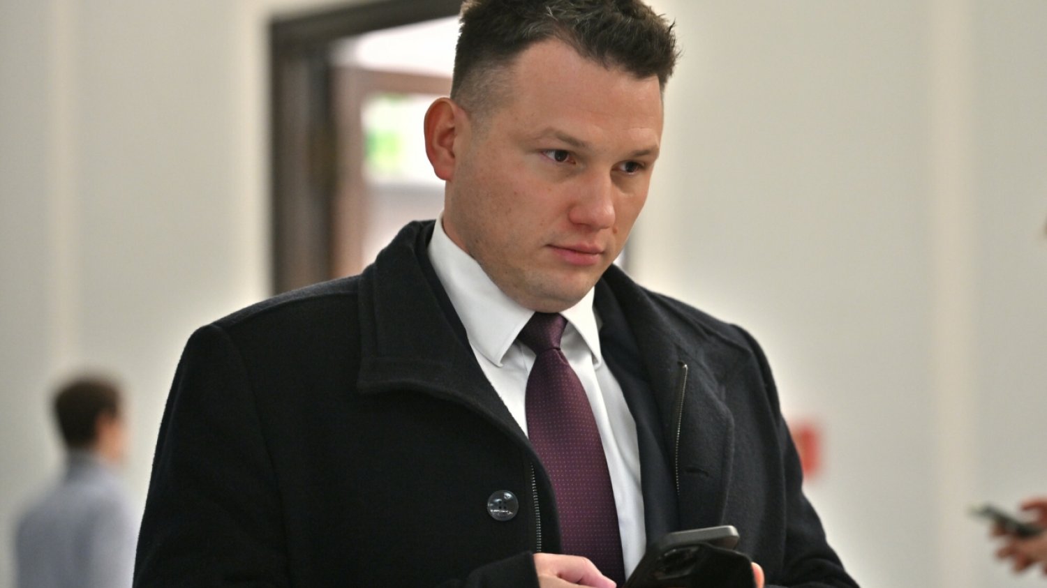 Sławomir Mentzen idący korytarzem Sejmu ze smartfonem w dłoni.