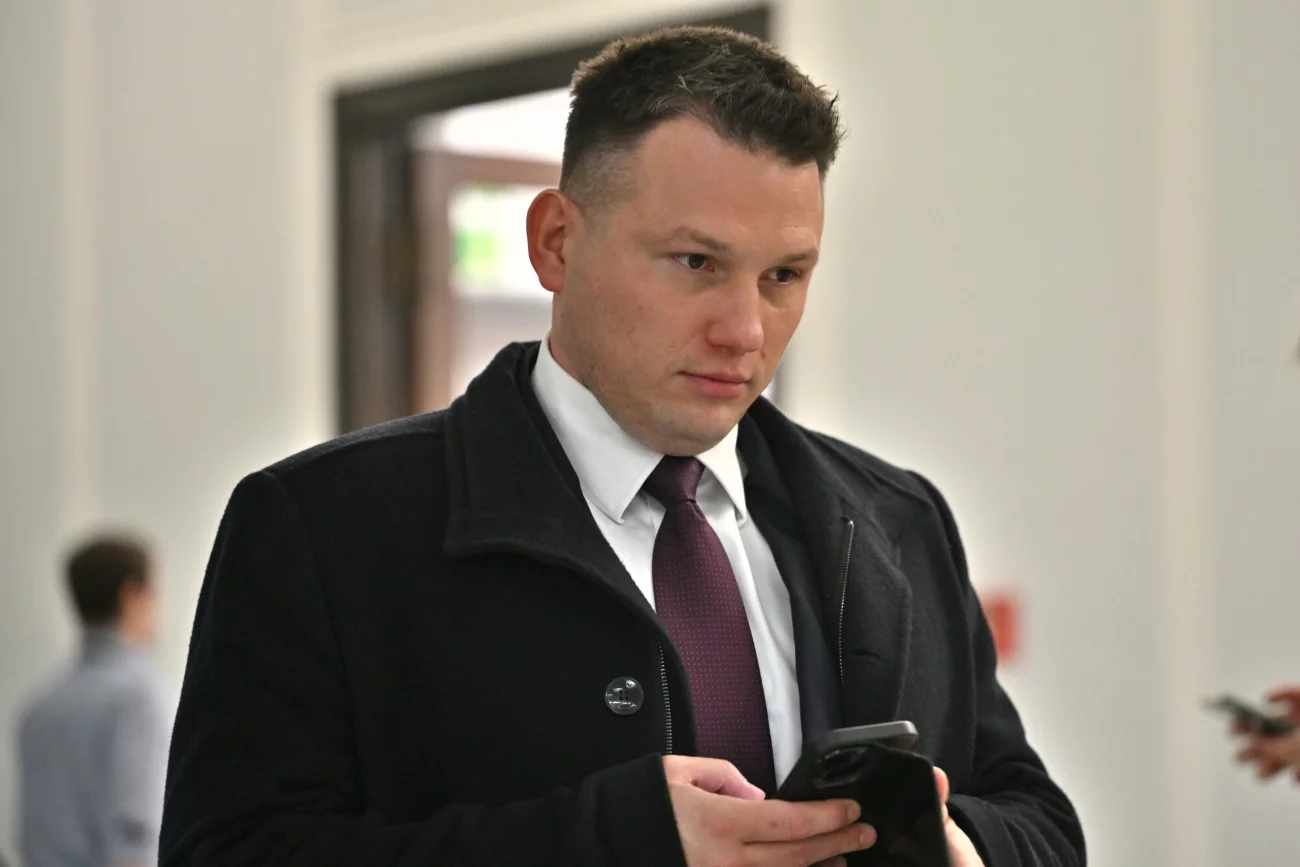 Sławomir Mentzen idący korytarzem Sejmu ze smartfonem w dłoni.