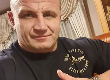 Mariusz Pudzianowski na tle suplementu diety z witaminą C, który poleca go do ochrony przed koronawirusem.
