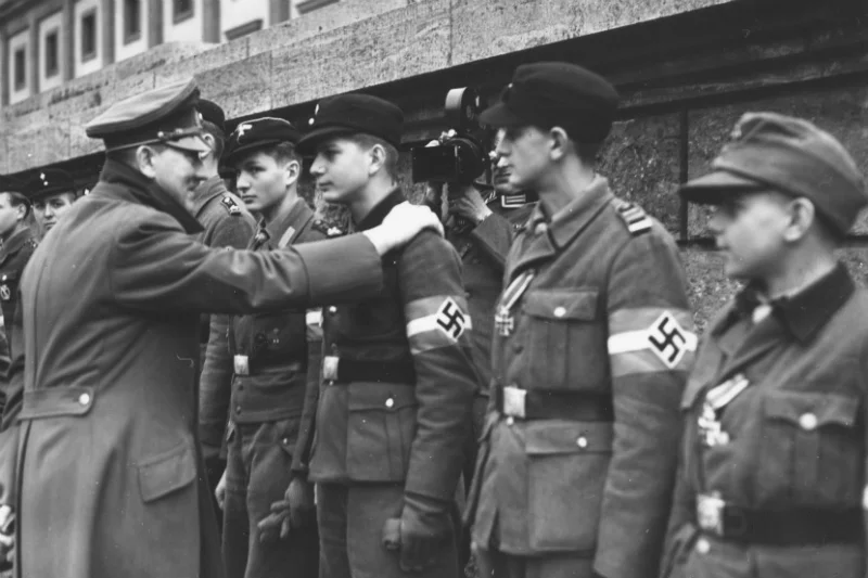Jedno z ostatnich oﬁcjalnych zdjęć Adolfa Hitlera. Przedstawia dekorowanie odznaczeniami członków Hitlerjugend, nastoletnich obrońców Berlina w dniu 20 kwietnia 1945 roku
