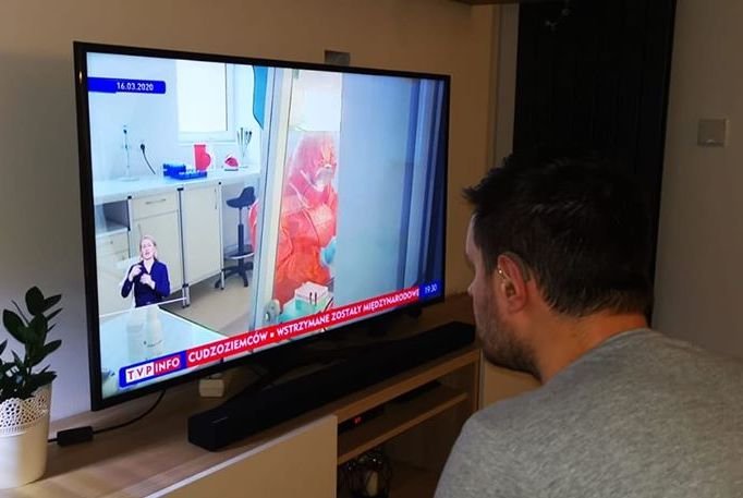 Głuchy ogląda w telewizji materiał na temat koronawirusa. Tłumacz polskiego języka migowego jak tak mały, że mężczyzna musi siedzieć tuż przy ekranie, by zrozumieć o co chodzi. Według badań UW osoba migająca powinna zajmować przynajmniej 1/8 ekranu.