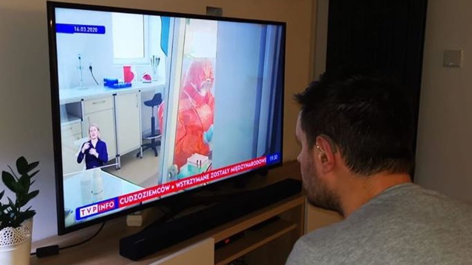 Głuchy ogląda w telewizji materiał na temat koronawirusa. Tłumacz polskiego języka migowego jak tak mały, że mężczyzna musi siedzieć tuż przy ekranie, by zrozumieć o co chodzi. Według badań UW osoba migająca powinna zajmować przynajmniej 1/8 ekranu.