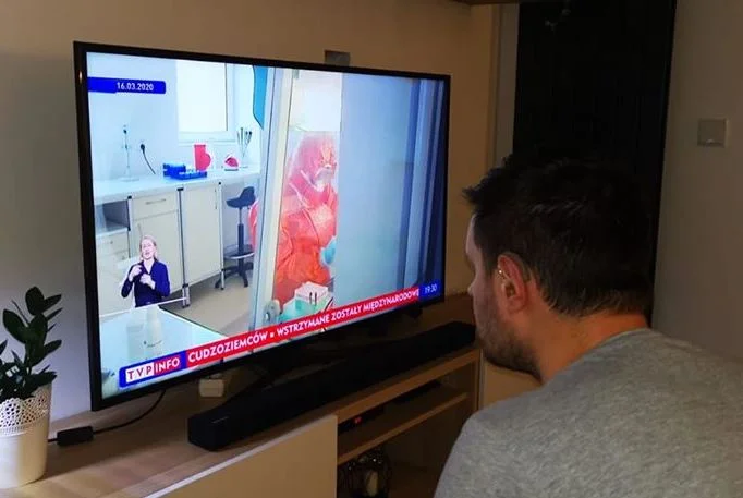 Głuchy ogląda w telewizji materiał na temat koronawirusa. Tłumacz polskiego języka migowego jak tak mały, że mężczyzna musi siedzieć tuż przy ekranie, by zrozumieć o co chodzi. Według badań UW osoba migająca powinna zajmować przynajmniej 1/8 ekranu.