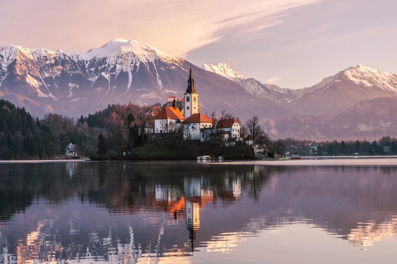 Widok na wyspę Blejski Otok na jeziorze Bled. W tle widać ośnieżone szczyty gór