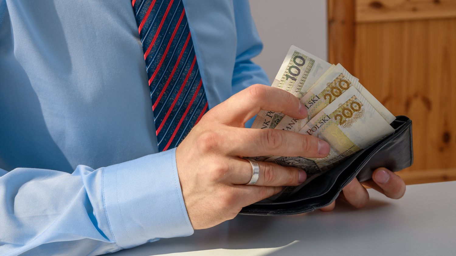 Mężczyzna w koszuli z krawatem wkładający pieniądze do portfela. Płaca minimalna 2027 i najniższa krajowa