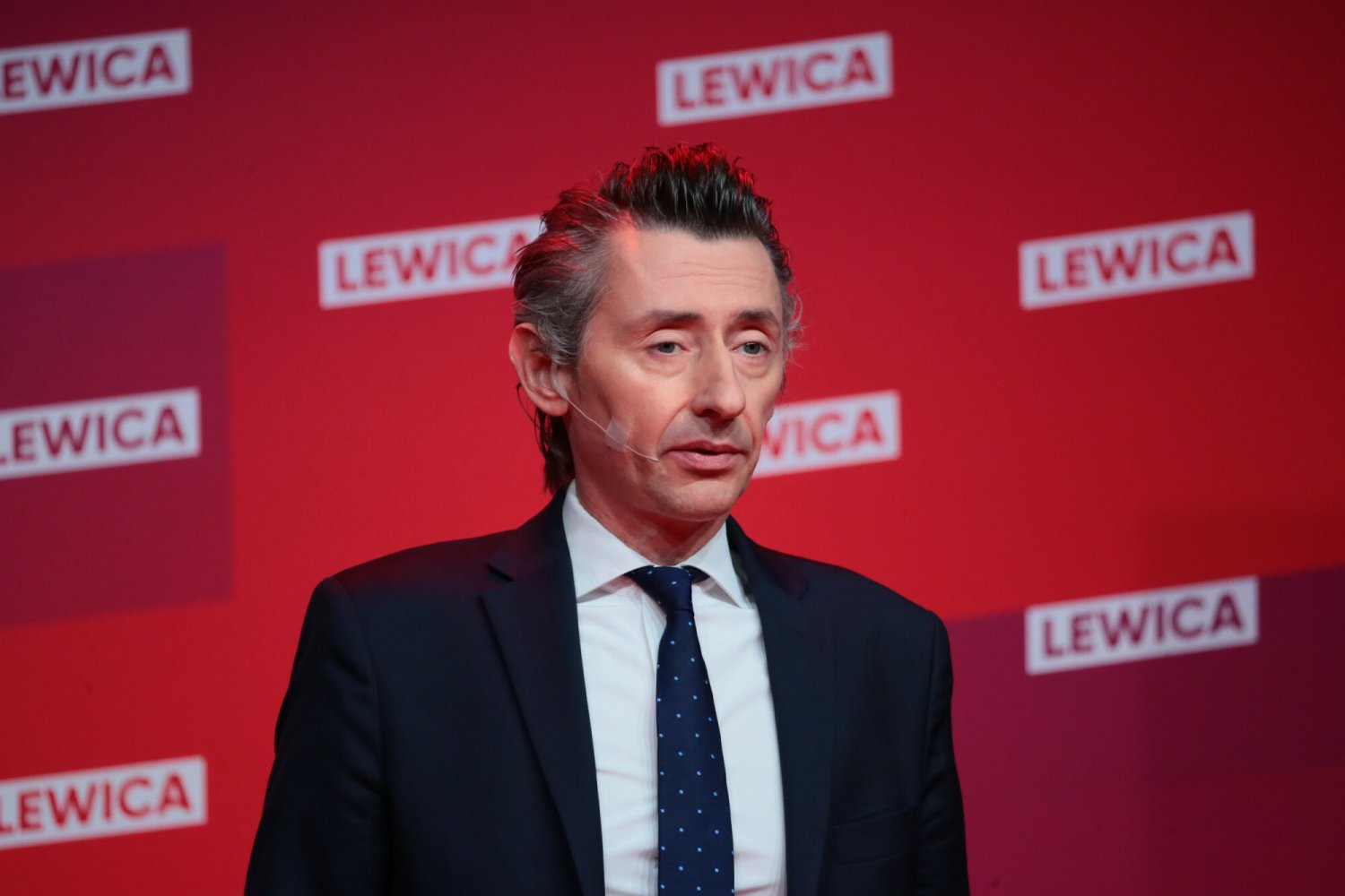 Maciej Gdula z Nowej Lewicy. W tle ścianka z logo koalicji Lewica, w której są też partia Razem, czy PPS.