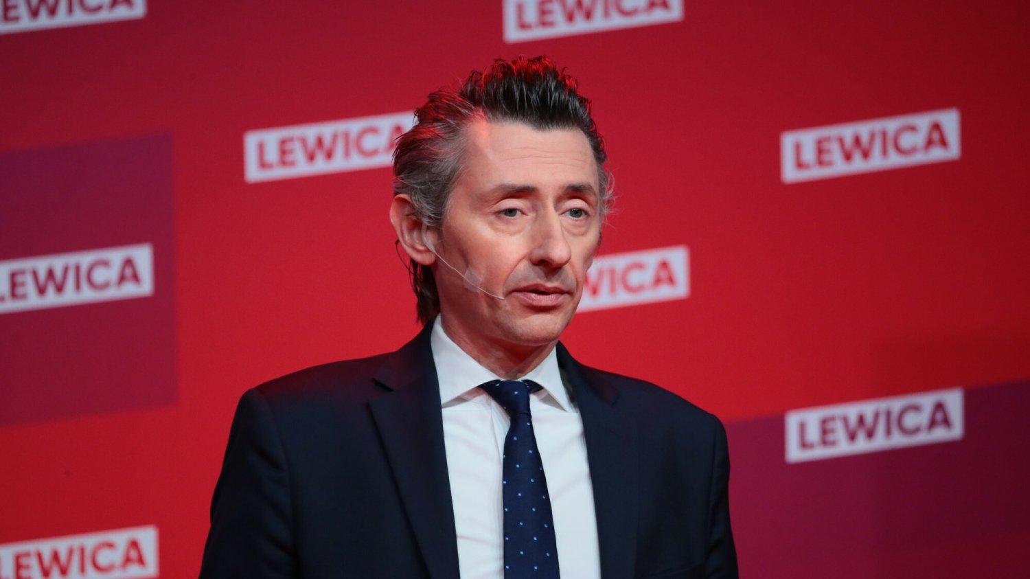 Maciej Gdula z Nowej Lewicy. W tle ścianka z logo koalicji Lewica, w której są też partia Razem, czy PPS.