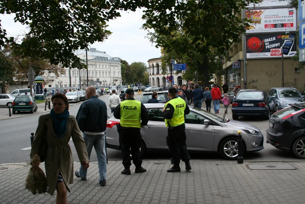 Patrol, ktory stoi z założonymi rękami przy aucie blokującym przejscie dla pieszych