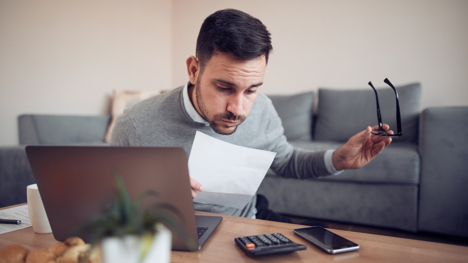 B2B bez optymalizacji jak teraz. Zmiany w ryczałcie i podatkach na 2027 Zmęczony mężczyzna pracujący przy laptopie w domowym biurze, przeglądający dokumenty i kalkulator. Zmiany w podatkach i wyższy ryczałt na B2B od 2027 roku.