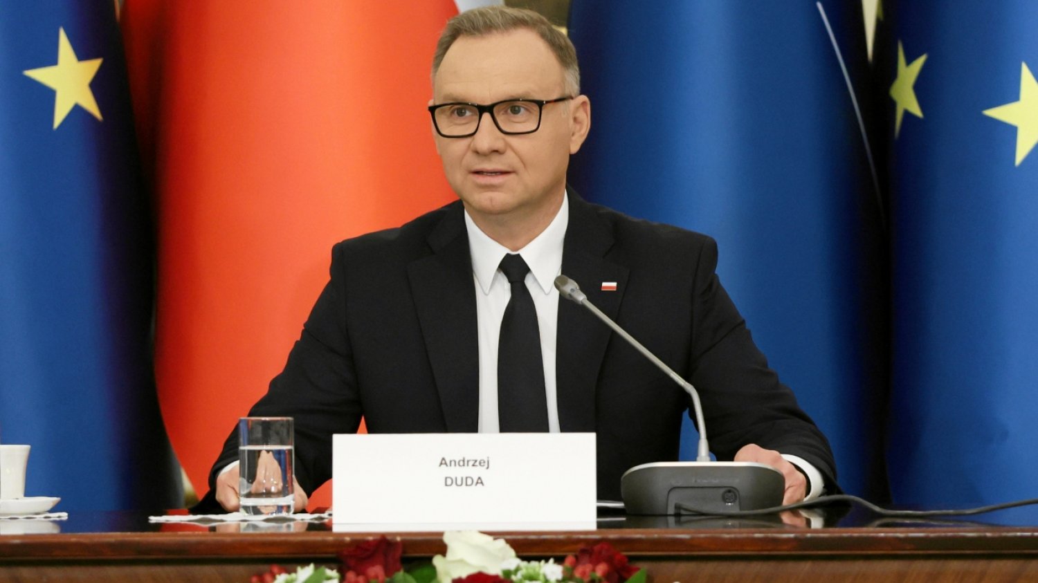 Prezydent Andrzej Duda siedzący przy stole na tle flagi Polski i Unii Europejskiej. Spotkanie Rady Bezpieczeństwa Narodowego.