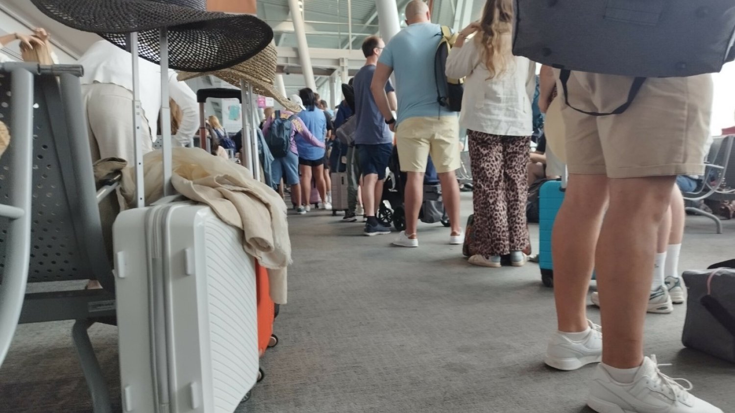 Walizki, kapelusze przeciwsłoneczne i podróżni czekający na lotnisku.