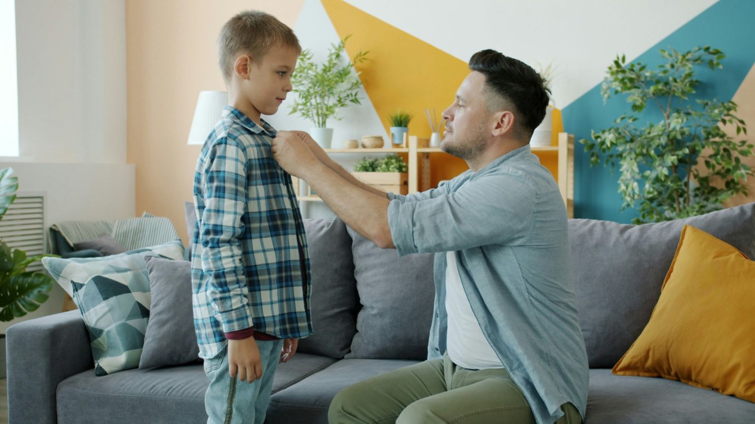 Plaga niesamodzielnych dzieci. Nadopiekuńczy rodzice robią im krzywdę. Mężczyzna zapinający guziki od koszuli chłopcu.