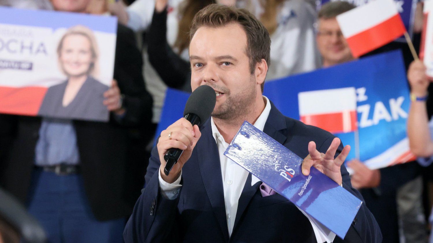 Rafał Bochenek, rzecznik prasowy Prawa i Sprawiedliwości, na konwencji wyborczej z podkładką z logo PiS w otoczeniu polityków obozu władzy.