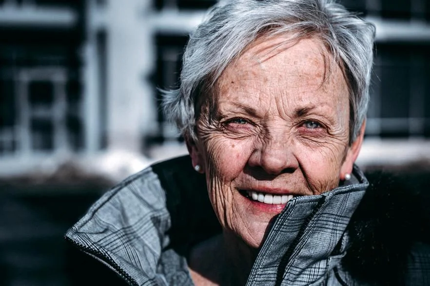 Twarz pogodnie uśmiechającej się, dojrzałej kobiety ze zmarszczkami w wieku powyżej 60 lat.