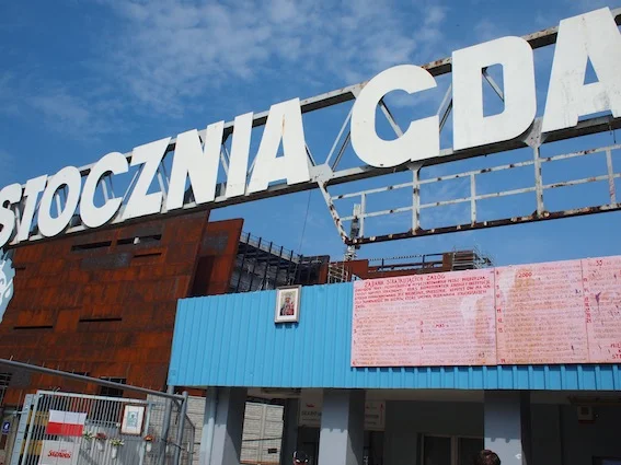 Brama do stoczni i postulaty sierpniowe, spisane na tablicach. W tle widać budynek powstającego muzeum. Zardzewiała bryła przypominająca skorodowany statek budzi kontrowersje, ale nam się podoba – nawiązuje do podobnych rozwiązań w Europie.
