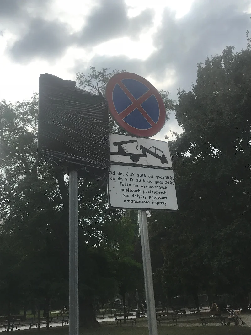 Widzimy zasłonięty znak parkingu i podstawiony ad hoc znak informujący o zakazie zatrzymywania się i odholowaniu na koszt właściciela pojazdu.