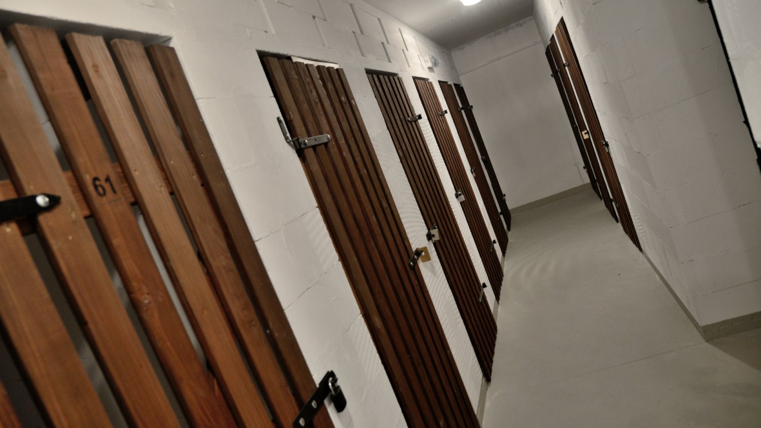 Biały korytarz z drewnianymi drzwiami do komórek lokatorskich w polskim bloku. Zgodnie z nowymi przepisami znowelizowanej ustawy takie piwnice mogą pełnić oficjalną funkcję punktu schronienia przed odłamkami.