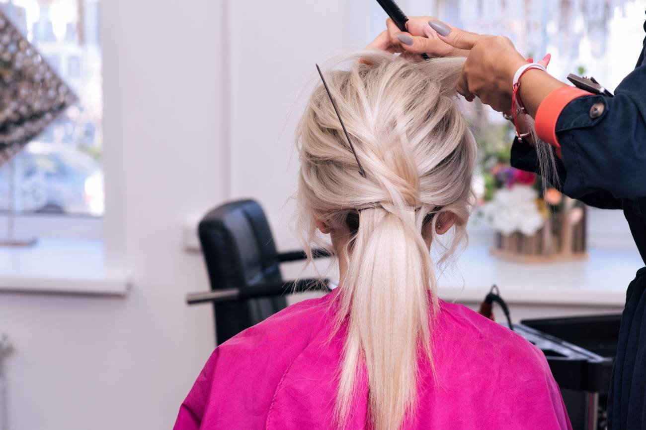 Kobieta z upiętymi włosami siedzi na fotelu. Ktoś robi jej fryzurę na specjalną okazję