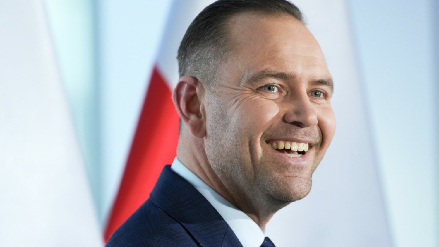 Karol Nawrocki na scenie, za nim biało-czerwona flaga Polski Karol Nawrocki