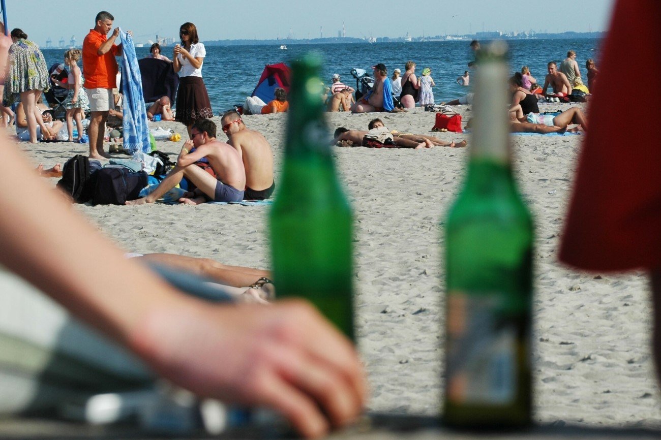 Ludzie na plaży w Gdyni. Na pierwszym planie dwie butelki piwa.