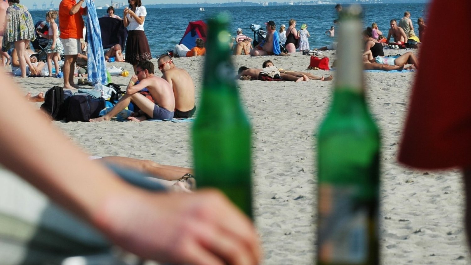 Ludzie na plaży w Gdyni. Na pierwszym planie dwie butelki piwa.