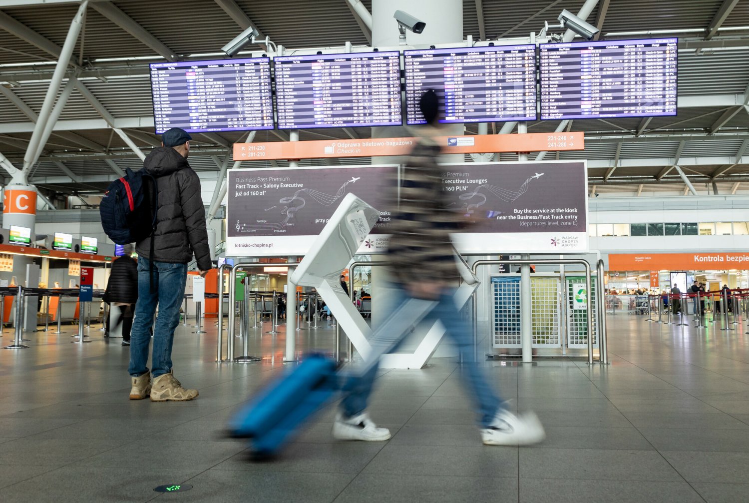 Na zdjęciu tablica odlotów i pasażerowi na polskim lotnisku