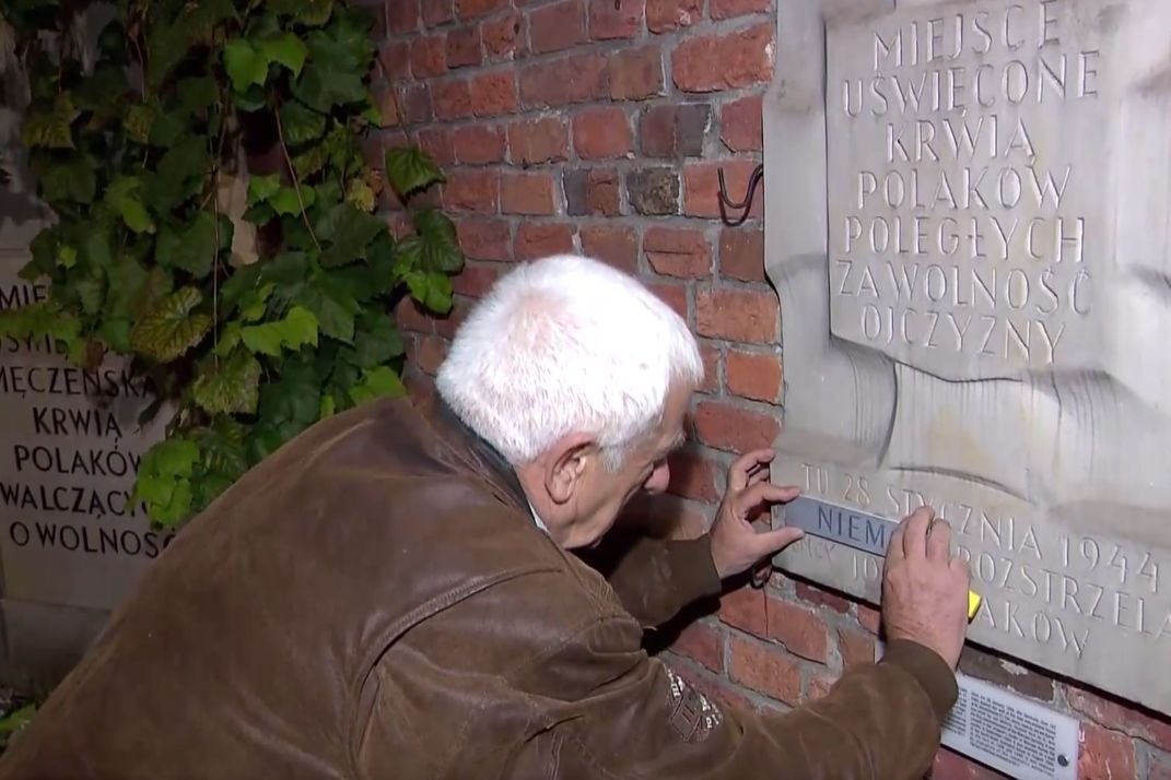 Jeden z ochotników, który w towarzystwie kamer TVP naklejał plakietkę na zabytkową tablicę.