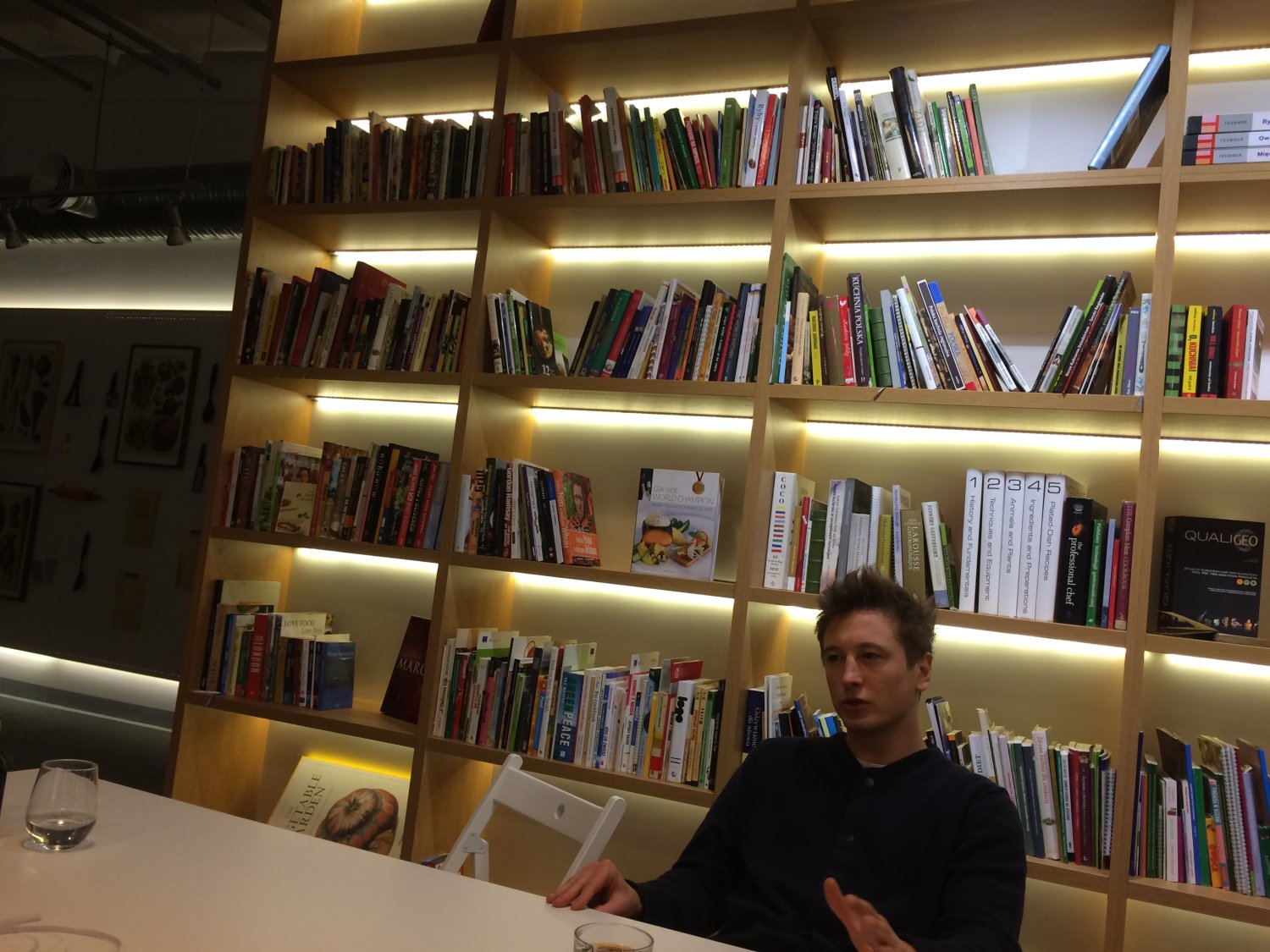 Grzegorz Łapanowski na tle powstającej biblioteczki najlepszych książek związanych z kulinariami.