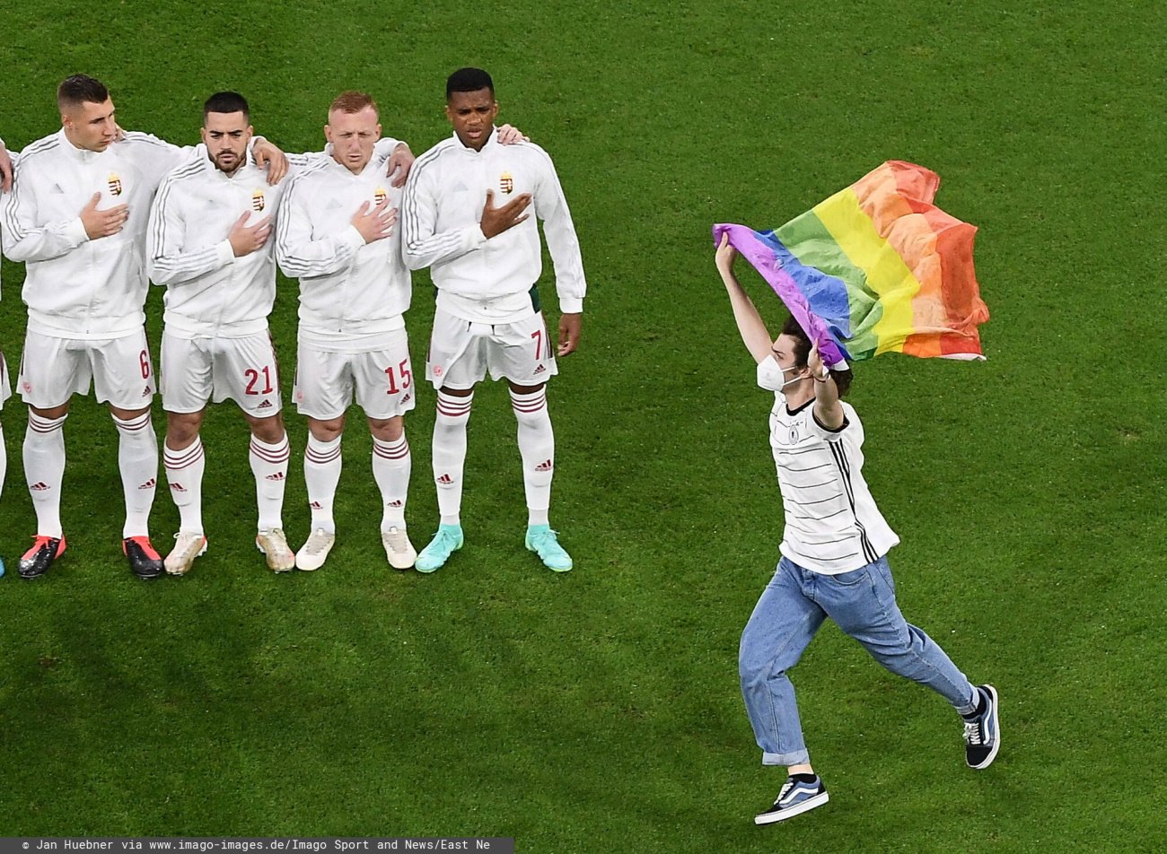 Młody chłopak z flagą w kolorach tęczy na murawie podczas hymnu Węgier