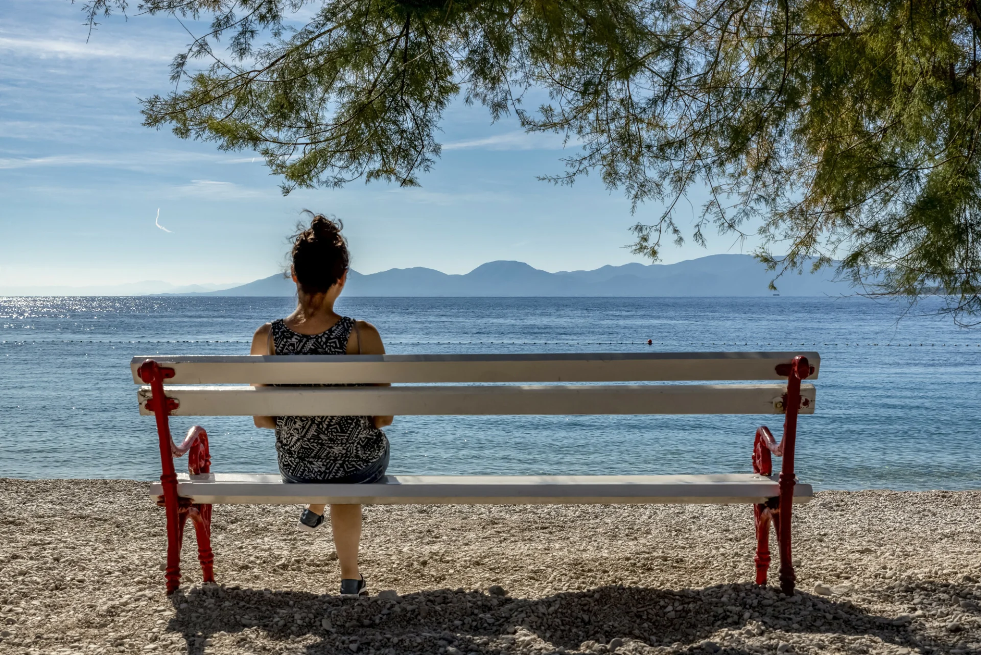 Wrzesień w Chorwacji. Kobieta siedzi w łagodnym słońcu na ławce na plaży i patrzy na Adriatyk.