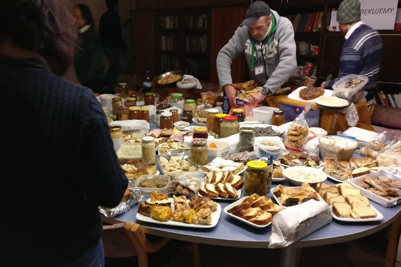 Katowice. Stół zastawiony dzięki akcji "Podzielmy się". Ta żywność trafiłaby do śmietników. Obdarowano nią podopiecznych Górnośląskiego Towarzystwa Charytatywnego. Z boku widać plakat z napisem: – "Dziękujemy".