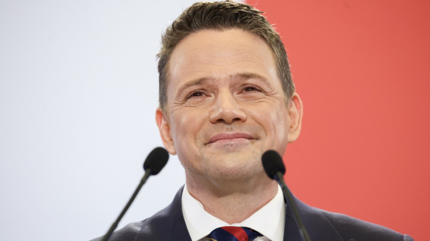 Rafał Trzaskowski na mównicy, w tle biało-czerwone tło Rafał Trzaskowski, prezydent Warszawy