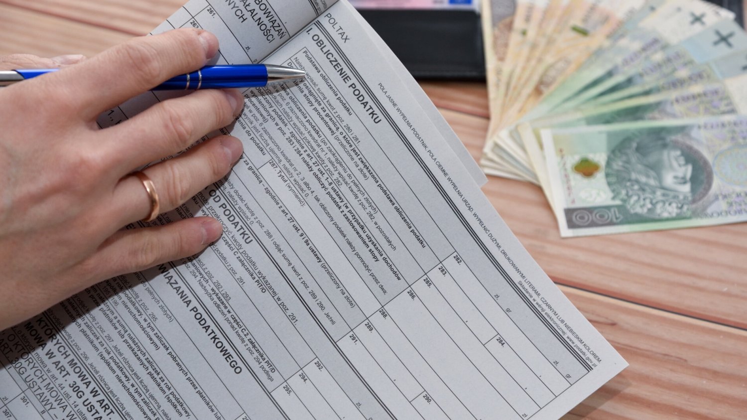 Kiedy zwrot podatku 2025? Tak szybciej dostaniesz pieniądze. Dłoń trzymająca długopis na formularzu zeznania podatkowego.