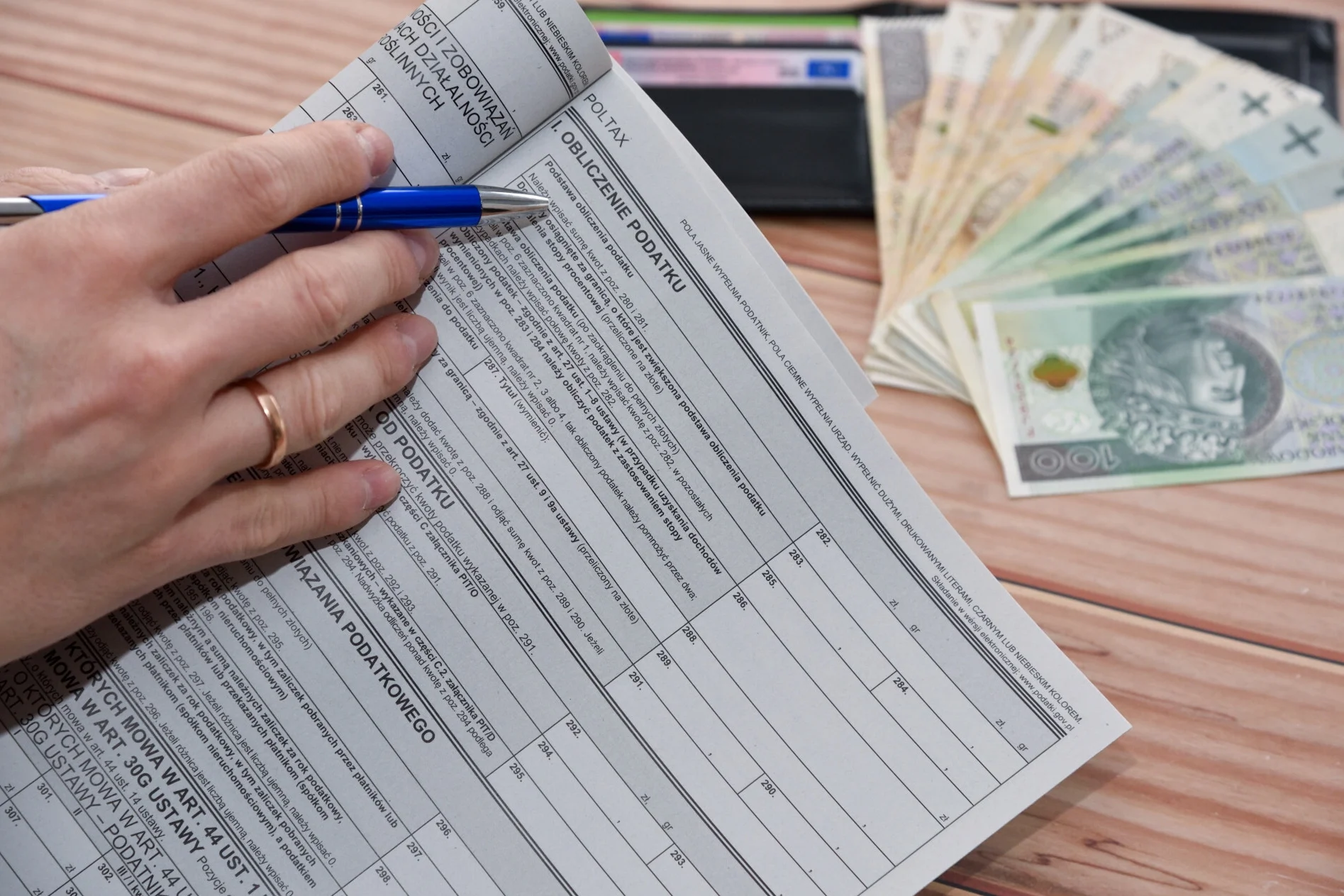 Kiedy zwrot podatku 2025? Tak szybciej dostaniesz pieniądze. Dłoń trzymająca długopis na formularzu zeznania podatkowego.