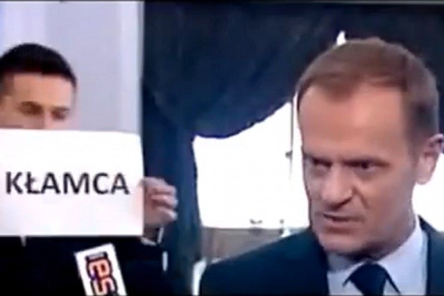 Poseł Marek Poznański stoi za plecami Donalda Tuska, pokazując kartkę z napisem "KŁAMCA"