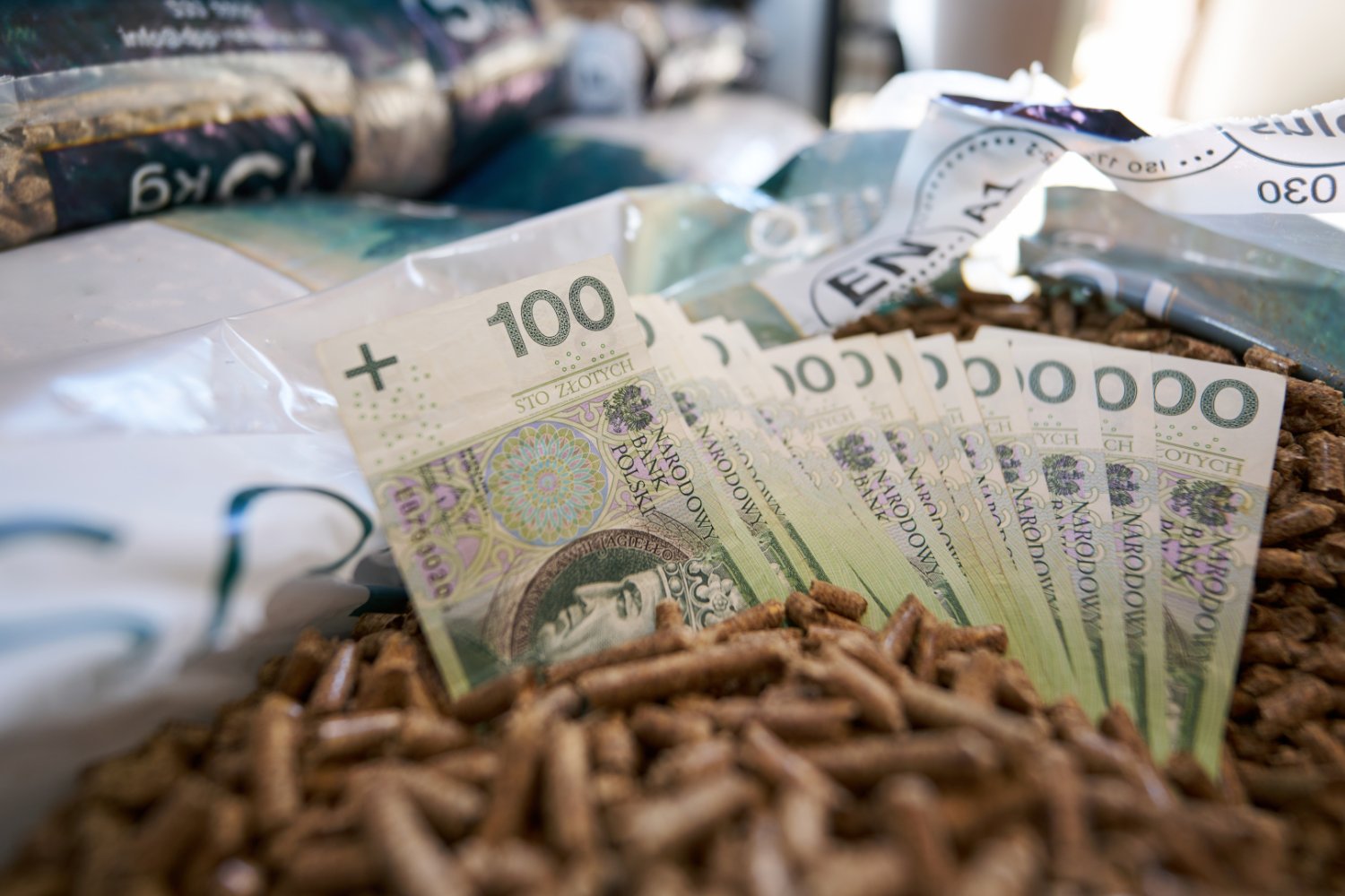 Banknoty stuzłotowe w granulacie pelletu symbolizujące wysoki koszt tego opału w Polsce