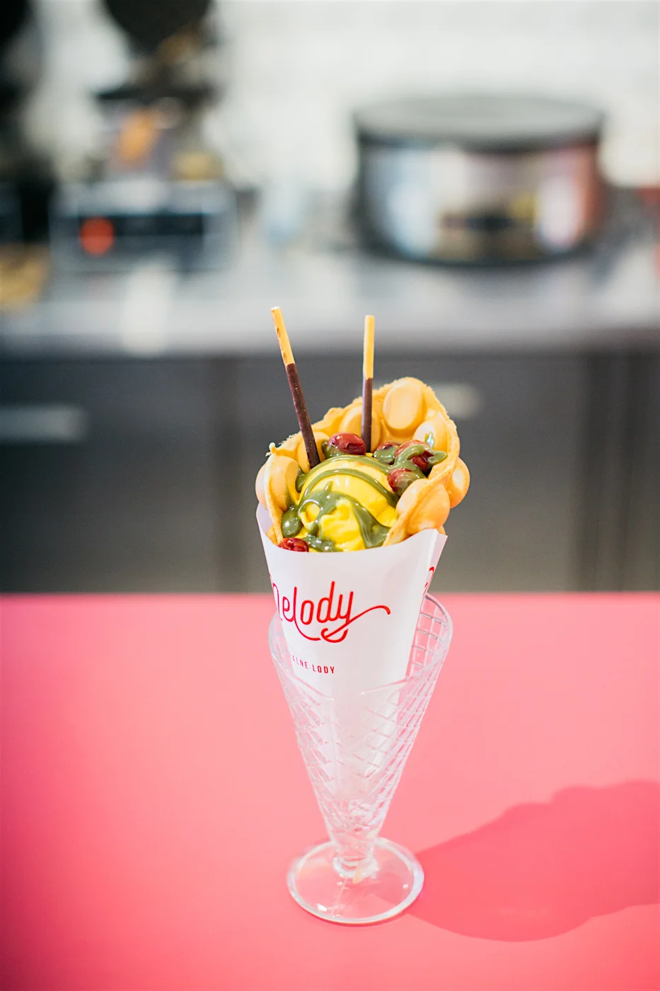 Gofr z lodami naturalnymi o smaku mango lassi, robioną na miejscu polewą o smaku matchy (zielonej herbaty) z wiśniami w zalewie i pałeczkami mikado