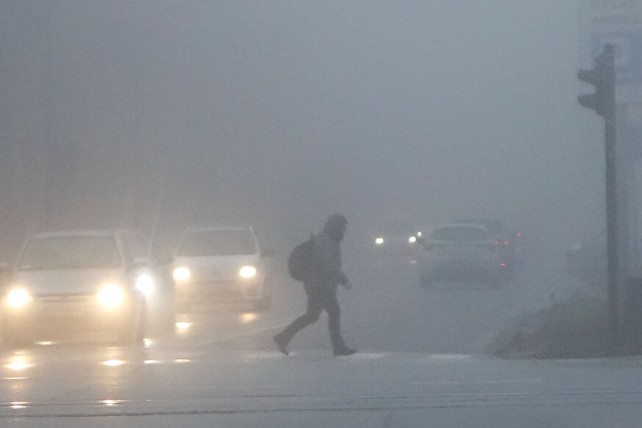 Pochmurno i mglisto: pogoda na sobotę 30 listopada Na zdjęciu osoba przechodząca przez zamgloną jezdnię w świetle reflektorów samochodów. Pogoda na sobotę 30 listopada: mgły w całej Polsce