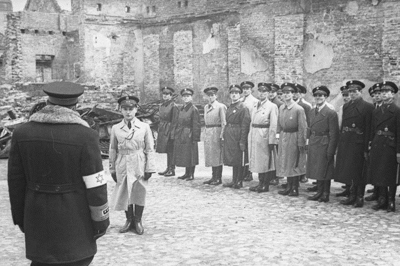 Józef Szeryński (stojący tyłem) odbiera meldunek Jakuba Lejkina, maj 1941 r., getto warszawskie.